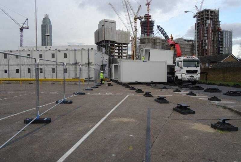 Modular building being installed at a construction site with urban skyline and cranes in the background