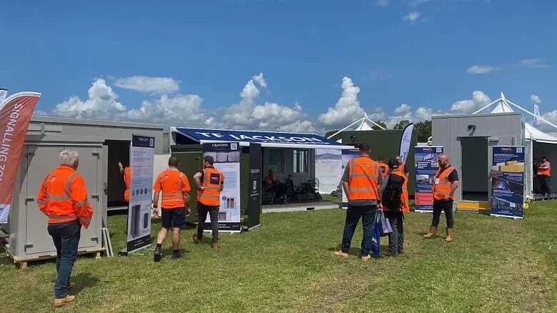 People in safety vests at a T.F. Jackson portable building exhibit on a sunny day.